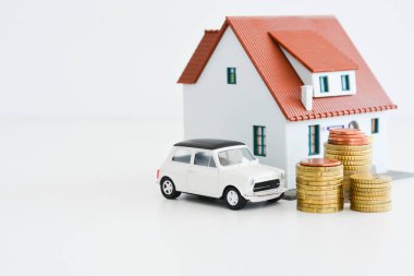 Beyaz arka plan üzerinde izole sikke yığını ile araba ve ev modeli