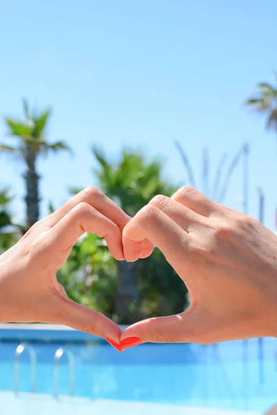 Manos en forma de corazón con una piscina y palmeras en el fondo —  Fotos de Stock