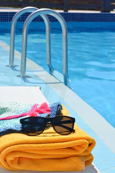 Γυαλιά ηλίου πετσέτα και ένα καπέλο κοντά σε μια πισίνα σε μια καυτή καλοκαιρινή μέρα — Φωτογραφία Αρχείου