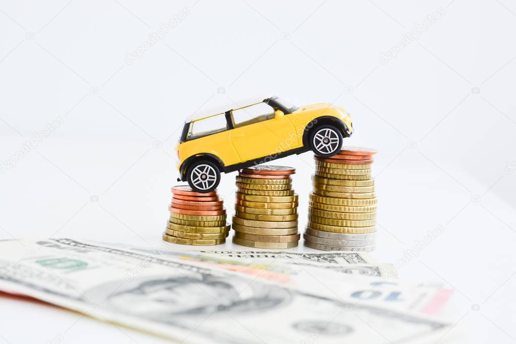 Yellow car climbing on pile of coins suggesting increase of sales trend