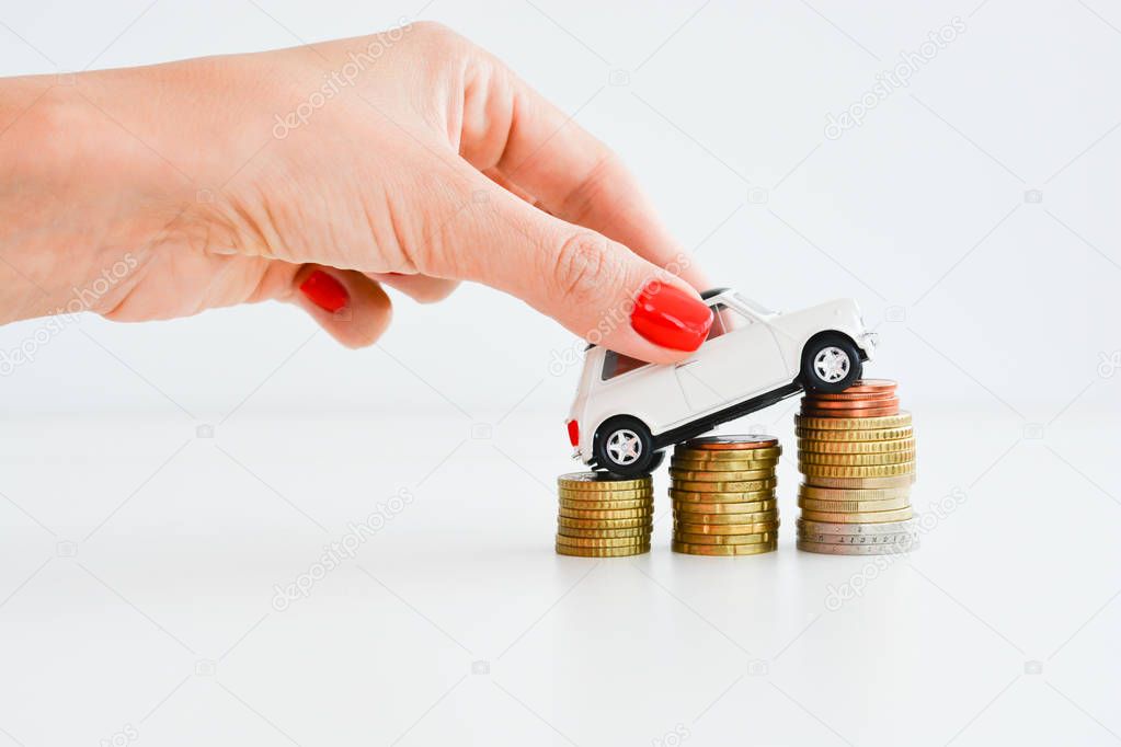 Woman hand pushing a toy car over a stack of coins
