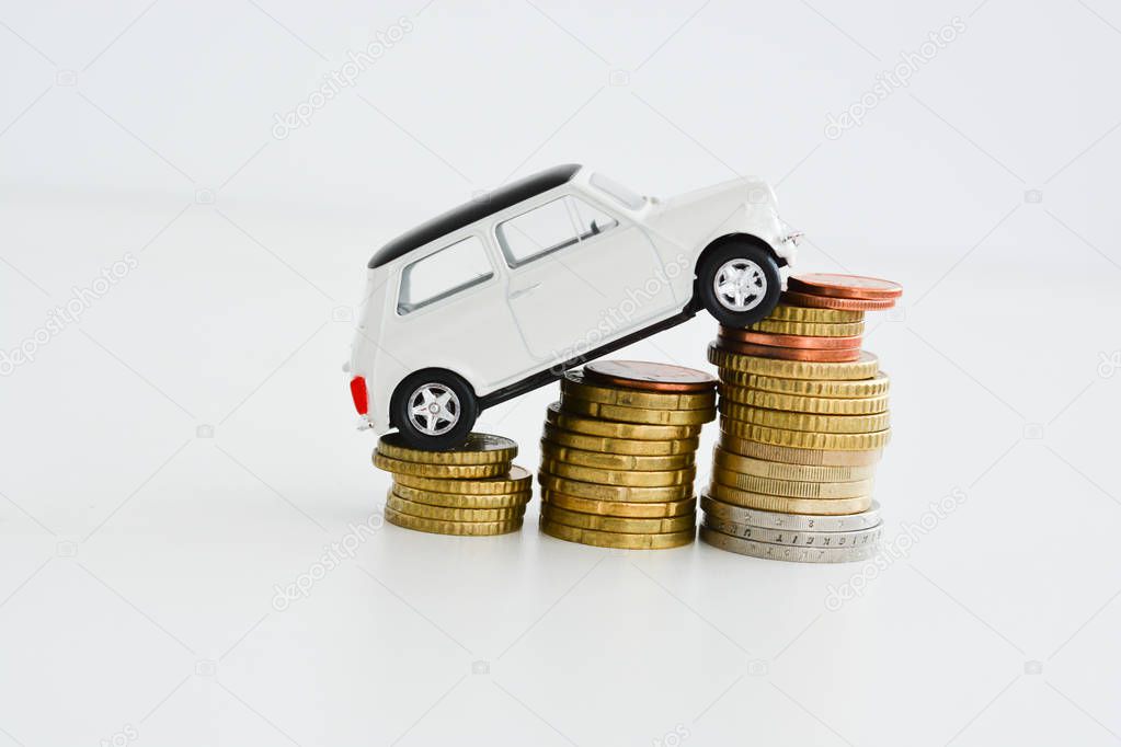 White car climbing on pile of coins suggesting increase of sales trend