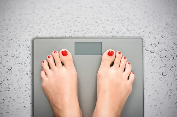 Ayuda a perder kilogramos con pies de mujer pisando una báscula de peso —  Fotos de Stock