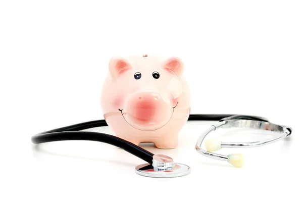 Salvadanaio e stetoscopio Isolati su sfondo bianco suggerendo risparmi per costi medici — Foto Stock