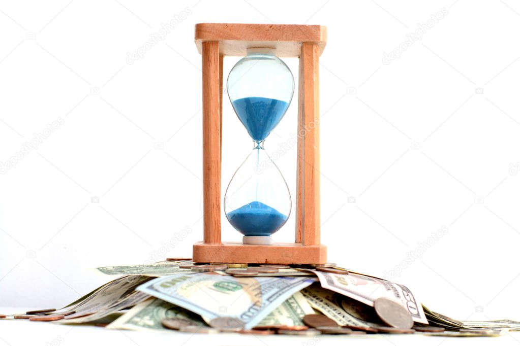 Sand pouring on hourglass standing on pile of money, suggesting deadline concept