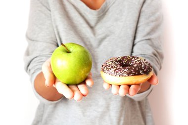 Diyet konsepti ile yeşil elma ve lezzetli çikolatalı çörek tutan genç kadın sağlıklı meyve ve tatlılar, arasında seçim yapma