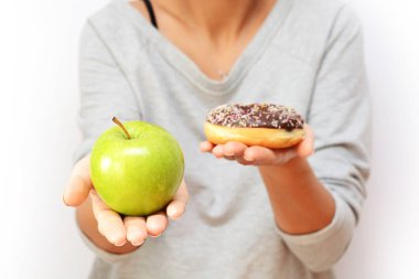 Diyet konsepti ile yeşil elma ve lezzetli çikolatalı çörek tutan genç kadın sağlıklı meyve ve tatlılar, arasında seçim yapma