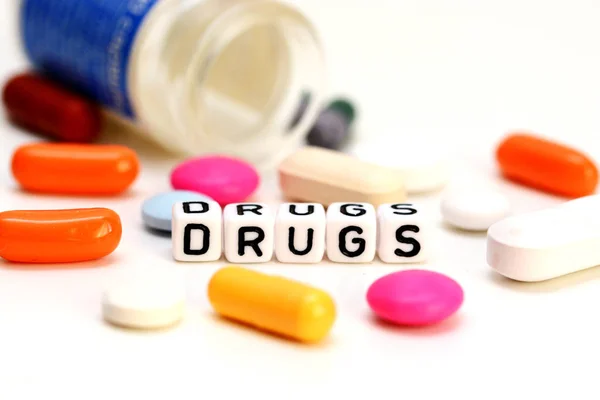 Цветные таблетки и наркотики слово изолированы на белом фоне — стоковое фото