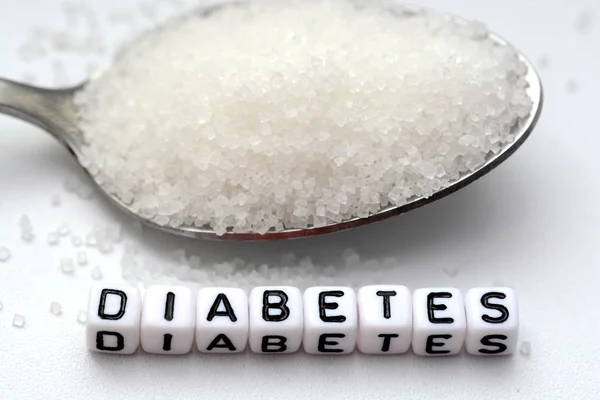 Cuentas de letras de plástico deletreando diabetes cerca de una cuchara llena de azúcar — Foto de Stock