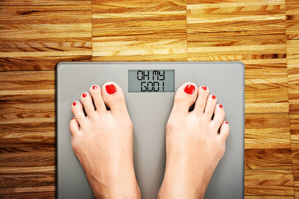Diet problems concept with woman feet on a weight scale displaying Oh my god phrase 