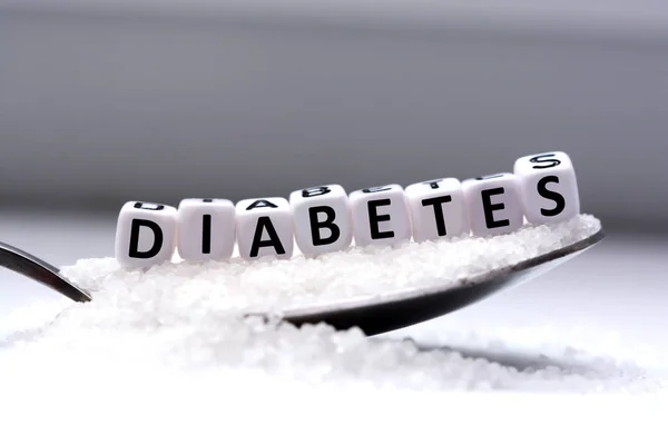 Cuentas de letras de plástico deletreando diabetes en una cuchara llena de azúcar — Foto de Stock