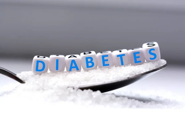 Cuentas de letras de plástico deletreando diabetes en una cuchara llena de azúcar — Foto de Stock