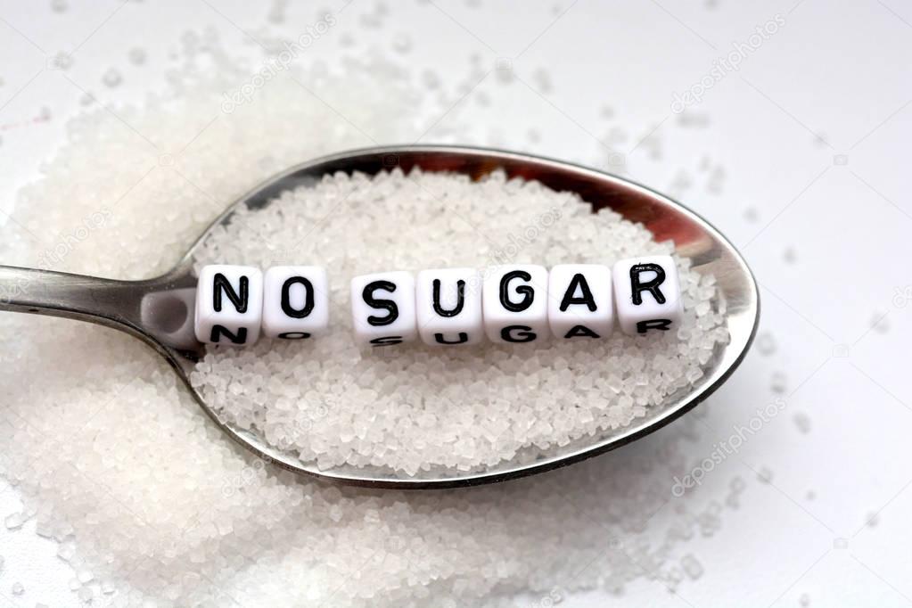 No sugar phrase made from plastic letter cubes placed in a spoon full of sugar