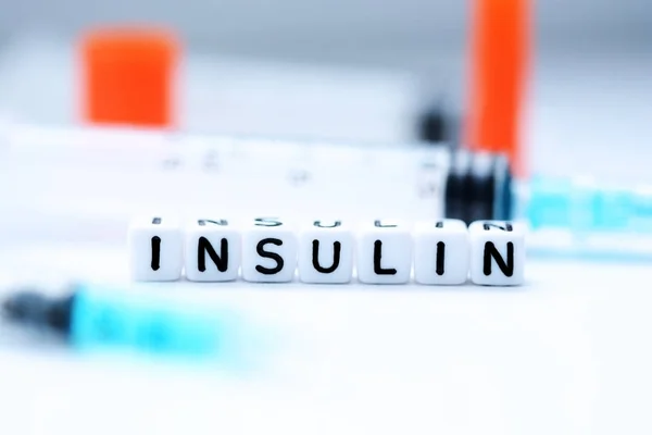 Слово "инсулин" пишется с пластиковыми бусами рядом со шприцем. — стоковое фото