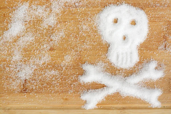 Dodelijke suikerverslaving voorgesteld door gemorste witte suiker kristallen vormen een schedel op een houten tafel — Stockfoto