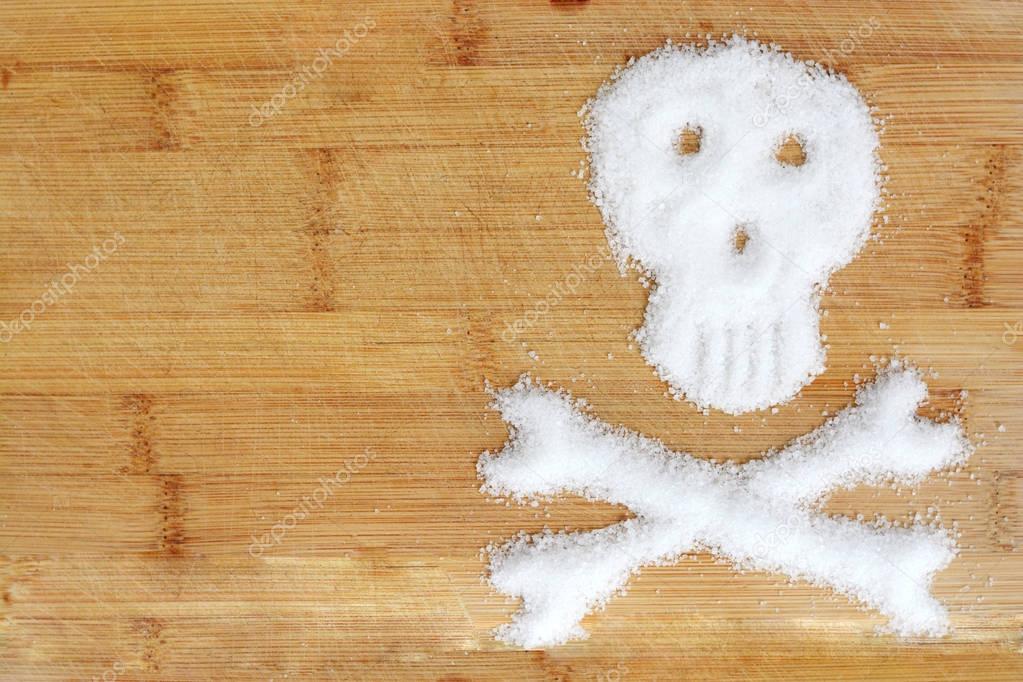 Deadly sugar addiction suggested by spilled white sugar crystals forming a skull on a wooden table