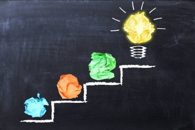 Evolving idea concept with colorful crumpled paper and light bulb on steps drawn on blackboard  clipart