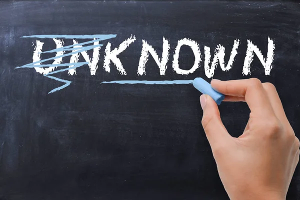 Woman changing the word unknown into known with chalk on blackboard — Stock Photo, Image