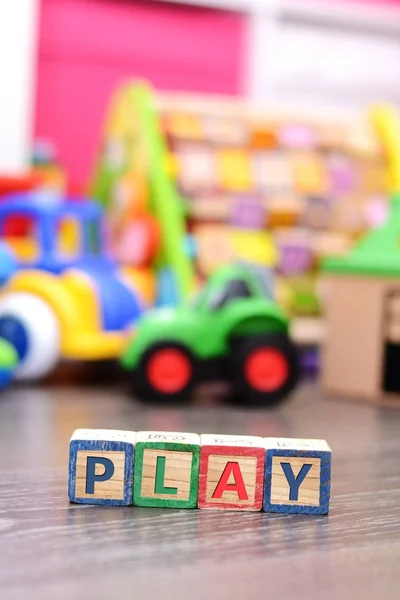 Играть слово из разноцветных кубиков с множеством игрушек на заднем плане — стоковое фото