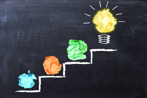 Evolving idea concept with colorful crumpled paper and light bulb on steps drawn on blackboard — Stock Photo, Image