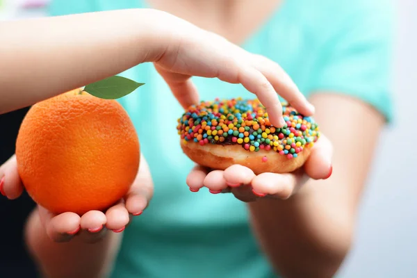 Kind overgewicht concept met meisje hand het kiezen van een zoete en ongezonde donut in plaats van een vrucht — Stockfoto
