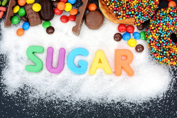 Cukr slovo napsané na pozadí bílého cukru se spoustou vícebarevné sladkosti — Stock fotografie