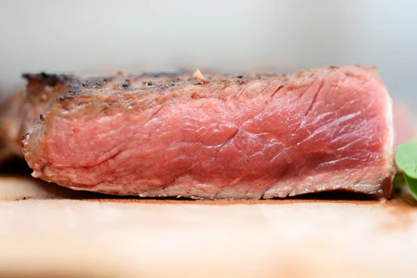 Filete a la parrilla medio cortado en rodajas sobre tabla de cortar de madera con hojas verdes y especias —  Fotos de Stock