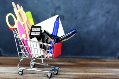 Geri okul kavramı - alışveriş sepeti ile kara tahta üzerinde okul malzemeleri için