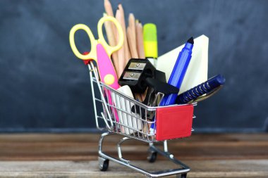Geri okul kavramı - alışveriş sepeti ile kara tahta üzerinde okul malzemeleri için