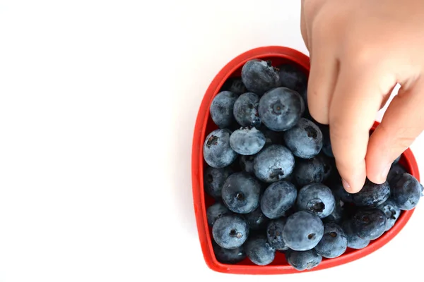 Child hand picking blueberries from a red heart shape bowl — Stock Photo, Image