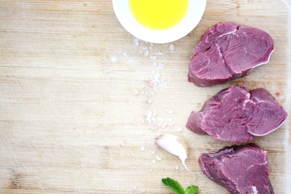 ヒマラヤの塩、ニンニク、白のボウルにオリーブ油を木製まな板の上の 3 つの新鮮な生の牛肉ステーキ — ストック写真