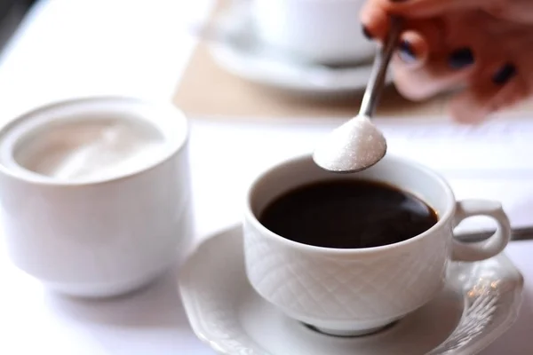 Woman hand adding a lot of sugar in a coffee from a sugar bowl, suggesting sugar overdose or unhealthy diet concept