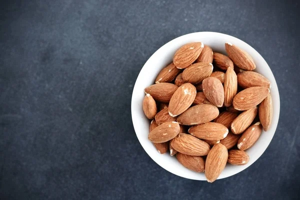 Whole almonds in white bowl isolated on dark background — Stock Photo, Image