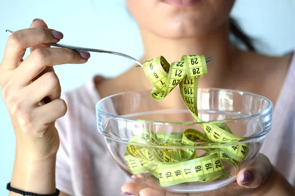 Giovane donna a dieta mangiare un nastro di misurazione giallo da una ciotola trasparente, immagine astratta — Foto Stock