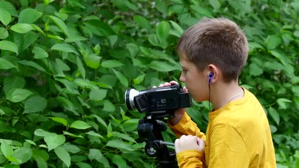 Jonge jongen kijkt in videocamera op achtergrond van groene park slow motion. — Stockvideo