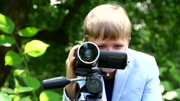 Jonge jongen kijkt in videocamera op achtergrond van groene park slow motion. — Stockvideo