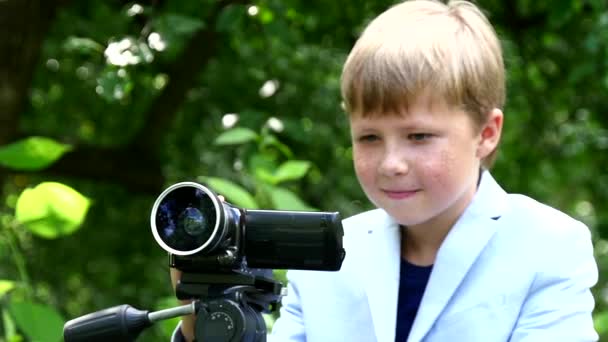 Jeune garçon avec caméra vidéo tourne un film sur la nature sur green park slow motion . — Video