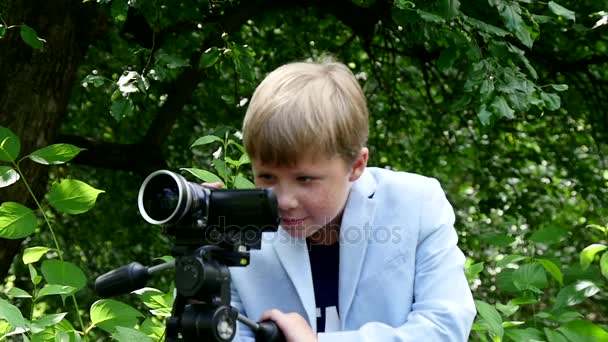 Niño con cámara de vídeo filma película sobre la naturaleza en el parque verde de cámara lenta . — Vídeo de stock