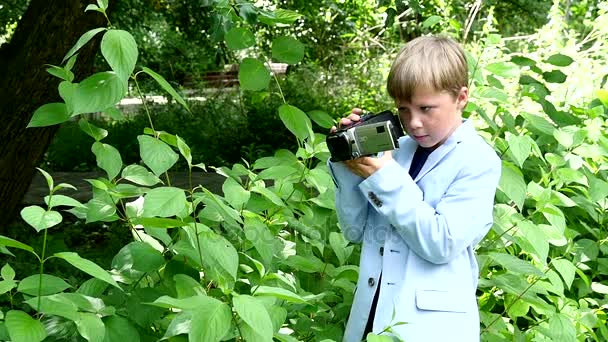 Niño con cámara de vídeo filma película en la naturaleza del parque verde de cámara lenta . — Vídeos de Stock