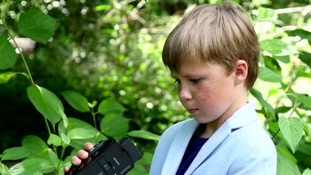 ビデオカメラの少年スローモーションの緑豊かな公園の自然の中の映画を撮影します。. — ストック動画