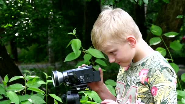 Jeune garçon avec caméra vidéo tourne le film dans la nature du parc vert au ralenti . — Video