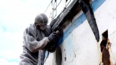 İşçiler tersanede tamirat sürecinde metali boyayla parçalıyorlar..