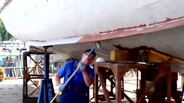 Pracovní maluje kovové spodní části lodi v loděnici v přístavu v Moskvě. — Stock video