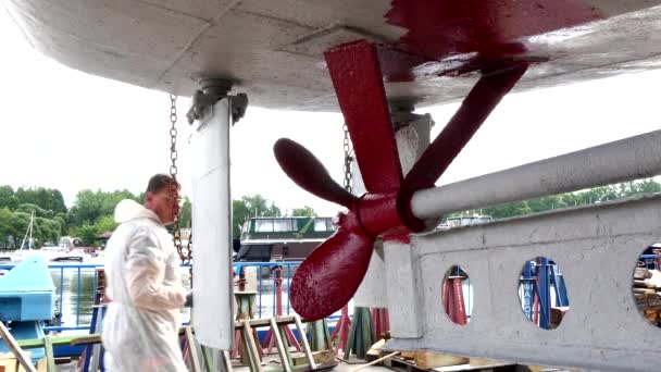 Worker paints metal of ship propeller red color at shipyard in port of Moscow. — Stock Video