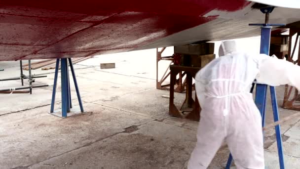El trabajador pinta el metal de la parte inferior del barco de color rojo en el astillero en el puerto . — Vídeos de Stock