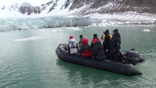 Lidé v lodi plout na pozadí hory sněhu v Severním ledovém oceánu Špicberky. — Stock video