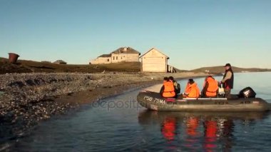People in rubber boat on background of abandoned houses New Earth Vaigach.