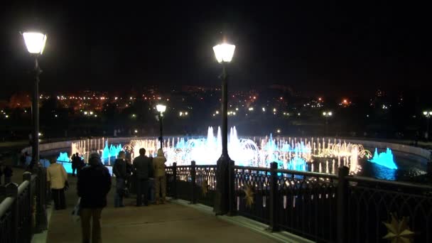 People walk at night near dancing fountains. — Stock Video