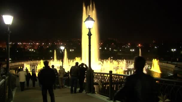Folk går på natten nära dansande fontäner. — Stockvideo