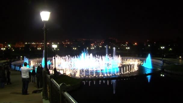 People walk at night near dancing fountains. — Stock Video